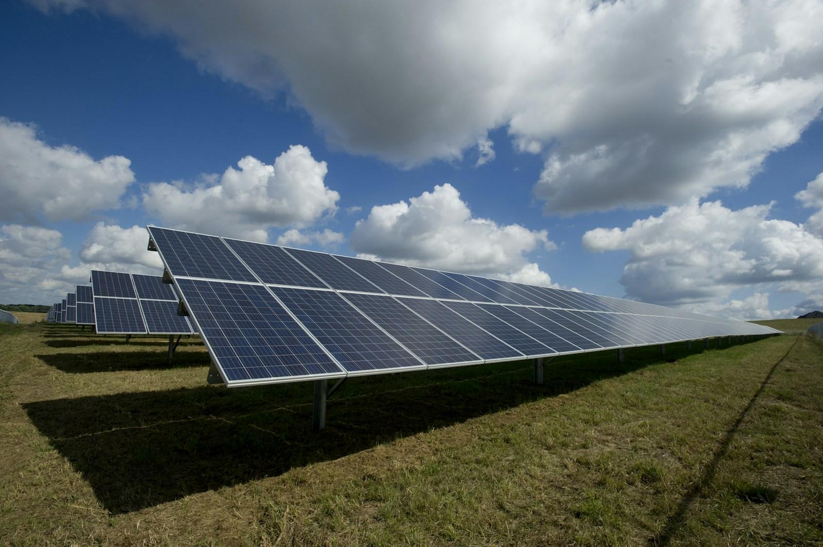 Rows of solar panels in a green field beneath a cloud-filled sky